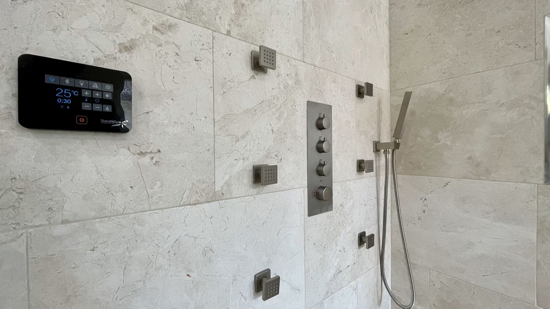 Shower with stone tile walls, control panel, showerheads, and handheld shower.