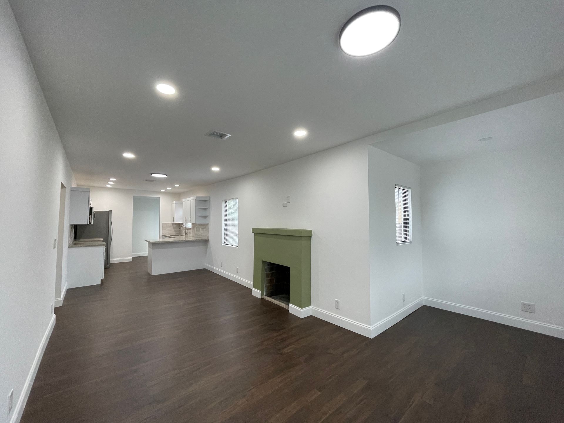 Spacious living room with dark wood floor, fireplace, white walls, and open kitchen.