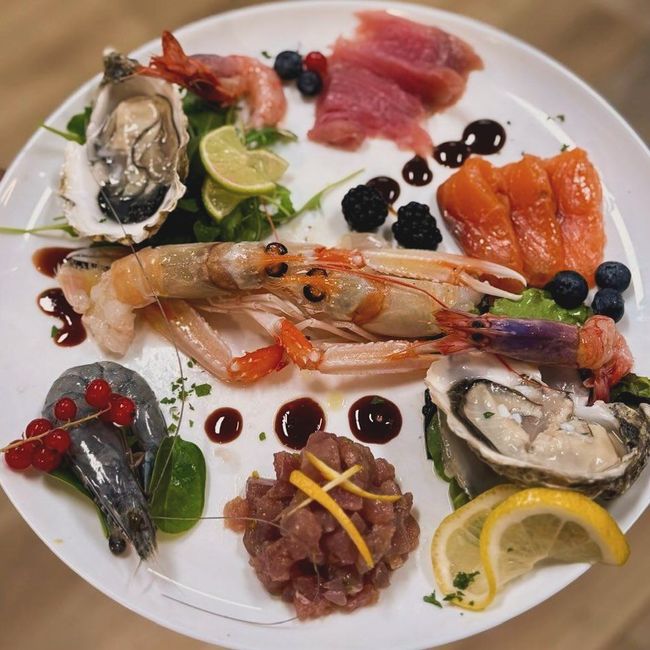 Piatto di frutti di mare: ostriche, gamberi, salmone, tonno e frutti di bosco disposti su un piatto bianco con salsa.