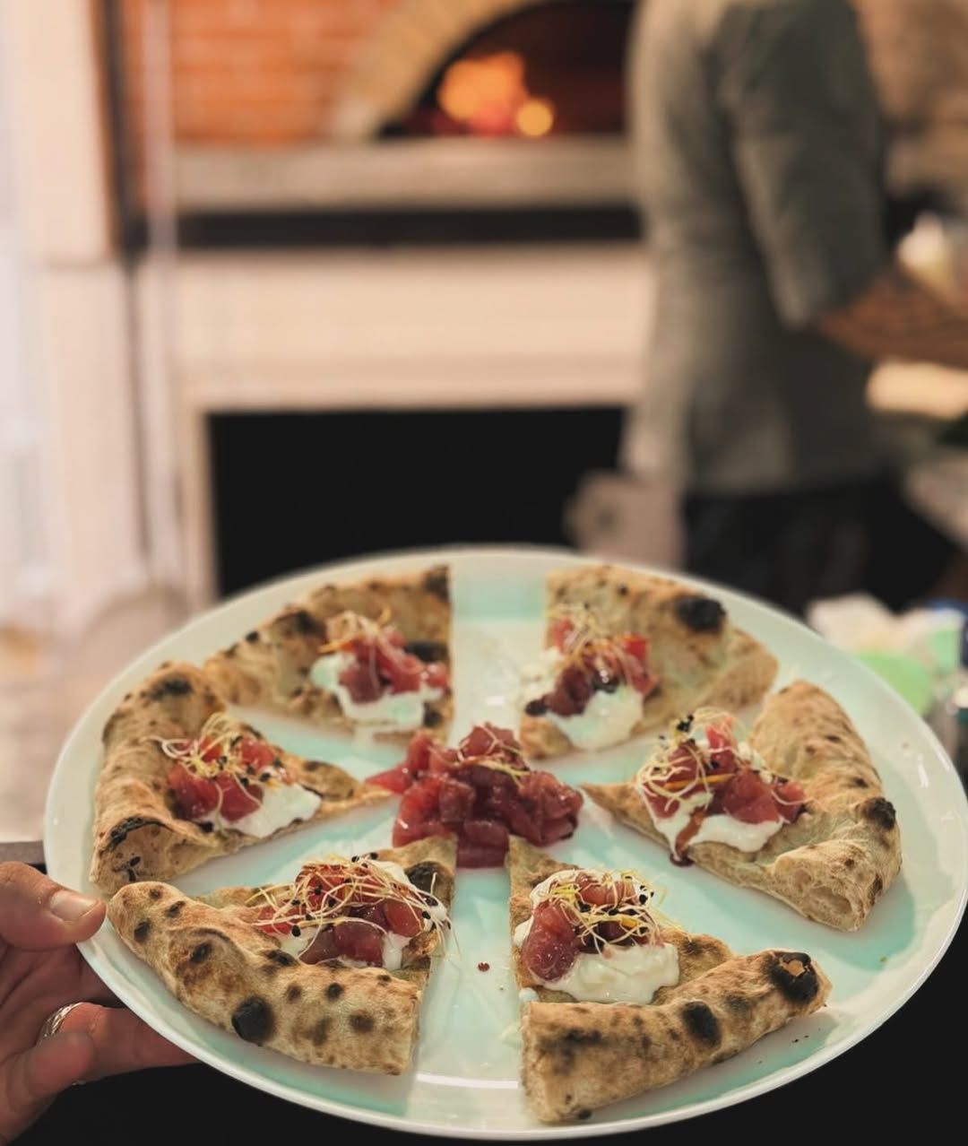 Un piatto di fette di pizza condite, tenuto davanti a un forno per pizza.