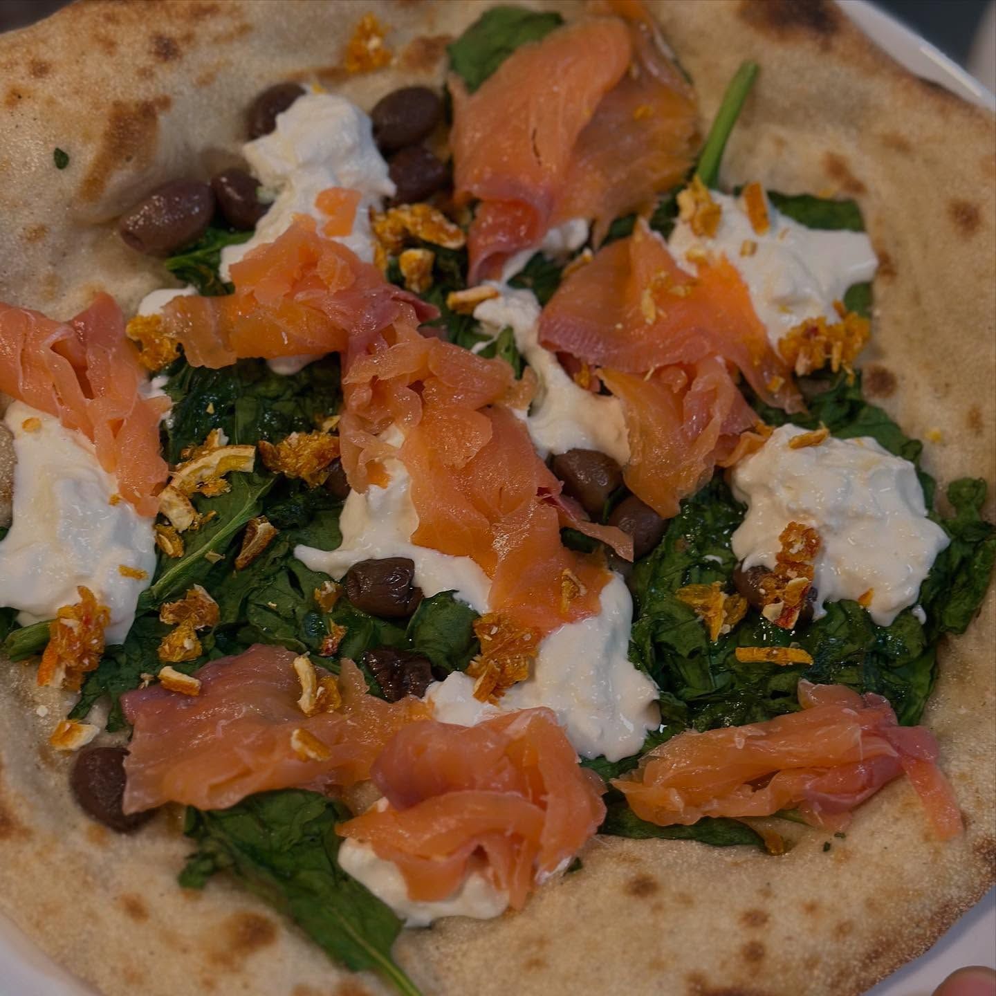 Pizza con salmone affumicato, ricotta, spinaci e olive.