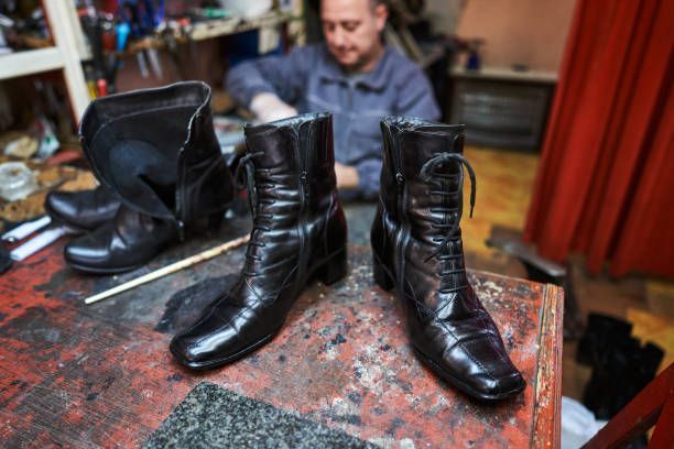 A man is working on a pair of black boots on a table.
