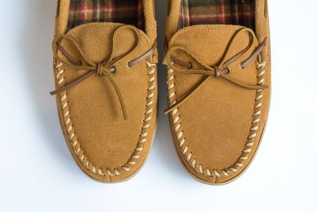A pair of brown slippers with a plaid lining on a white surface.