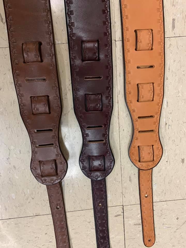 Three leather guitar straps are sitting on a tiled floor.