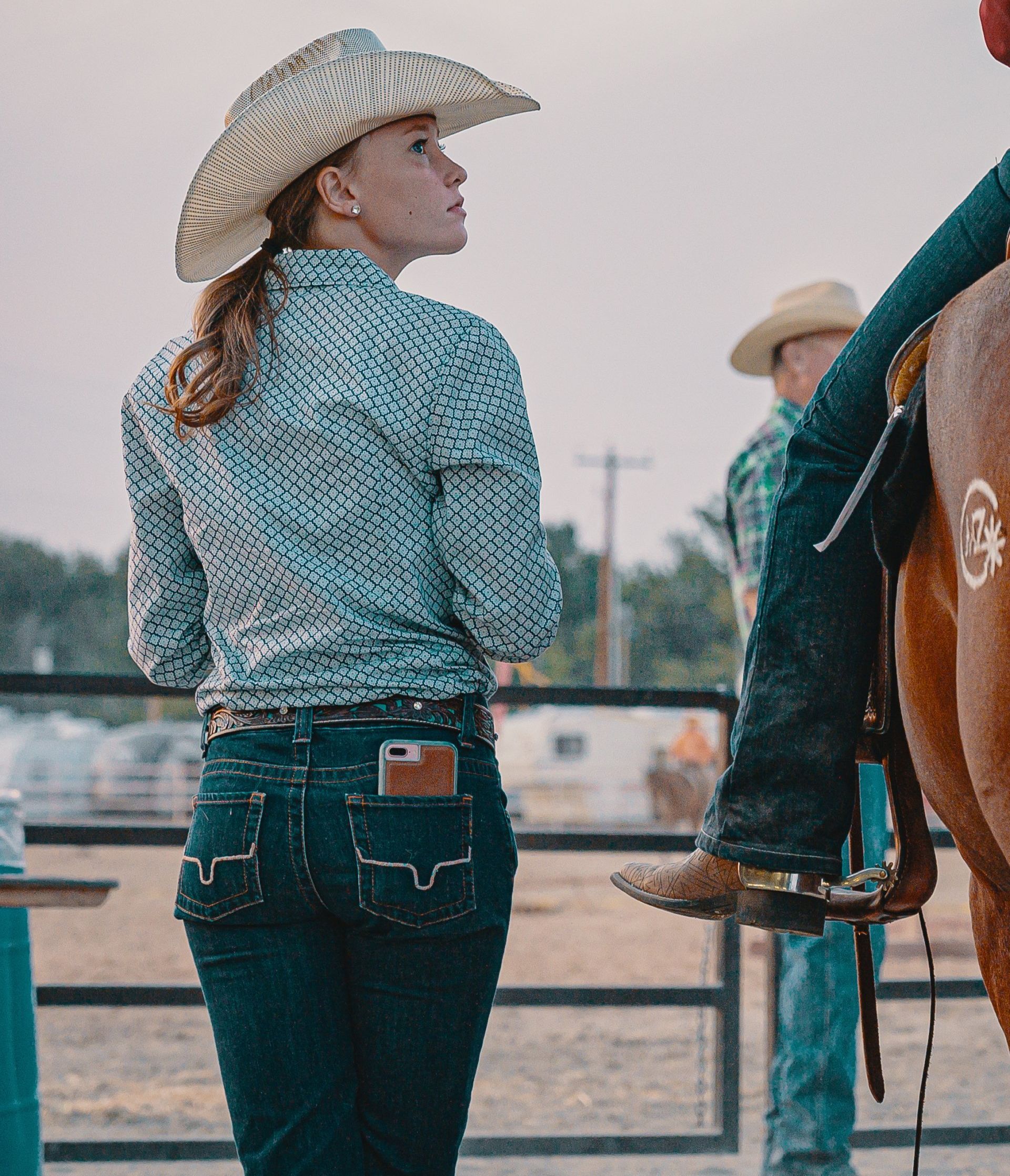 A woman wearing a cowboy hat is standing next to a man riding a horse.