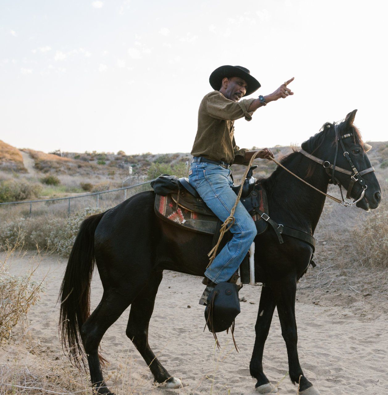 A man in a cowboy hat is riding a black horse