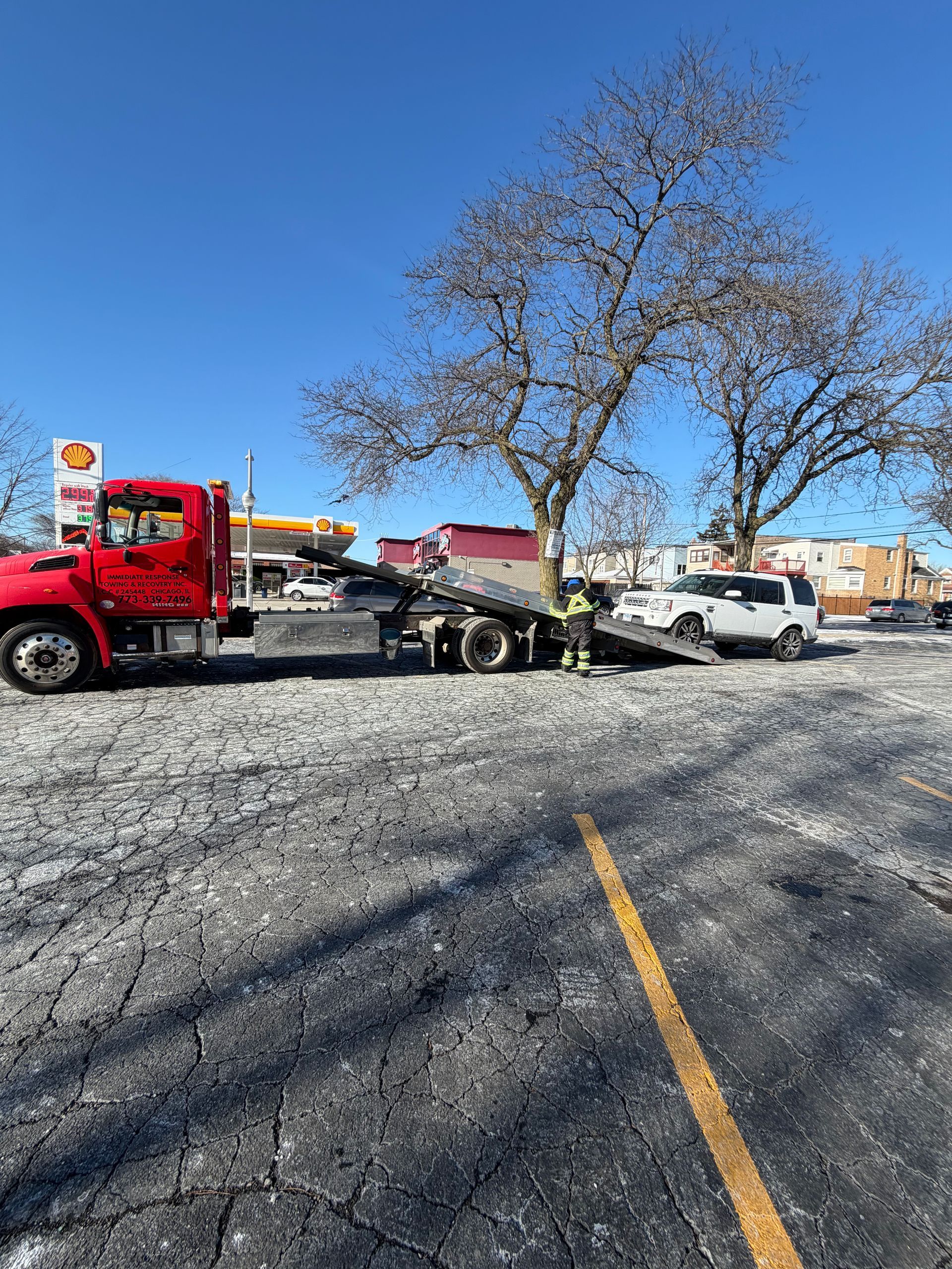 A red tow truck loading a white car onto its flatbed in a parking lot on a sunny day.