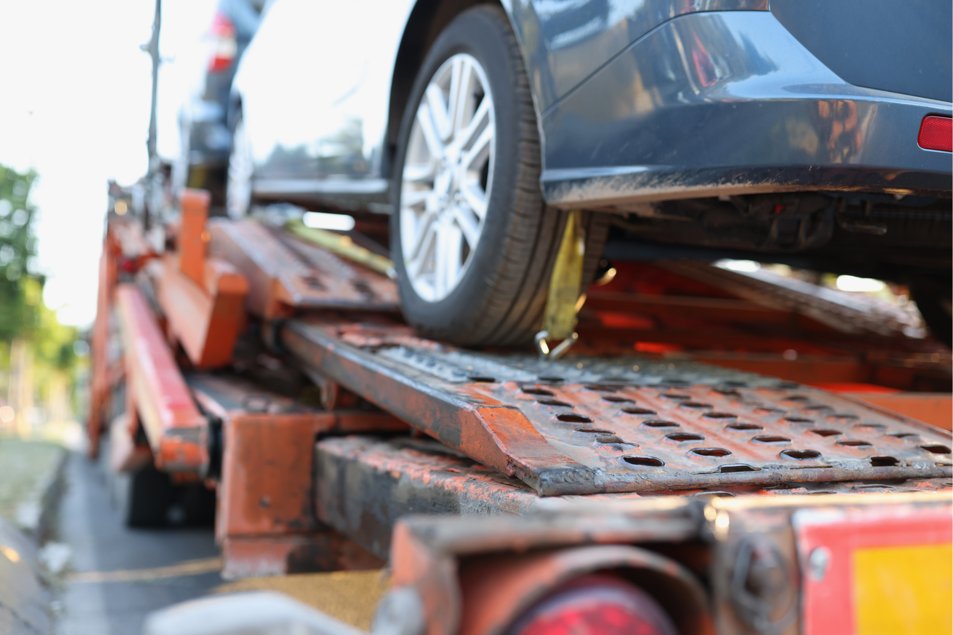 Car being loaded onto a rusty tow truck's ramp; vehicle's tire visible.
