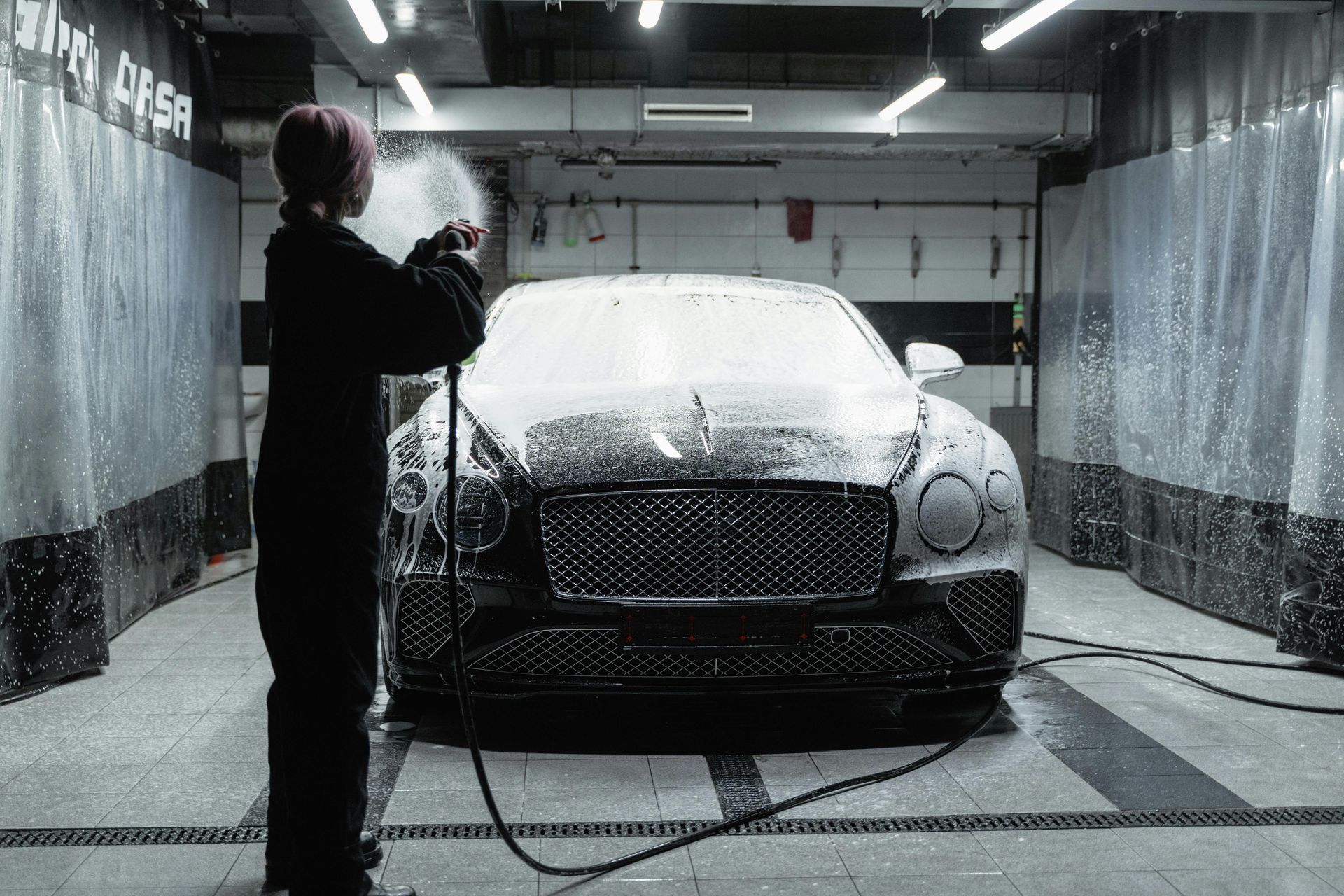 Person washes a black Bentley with foamy spray at a car wash.