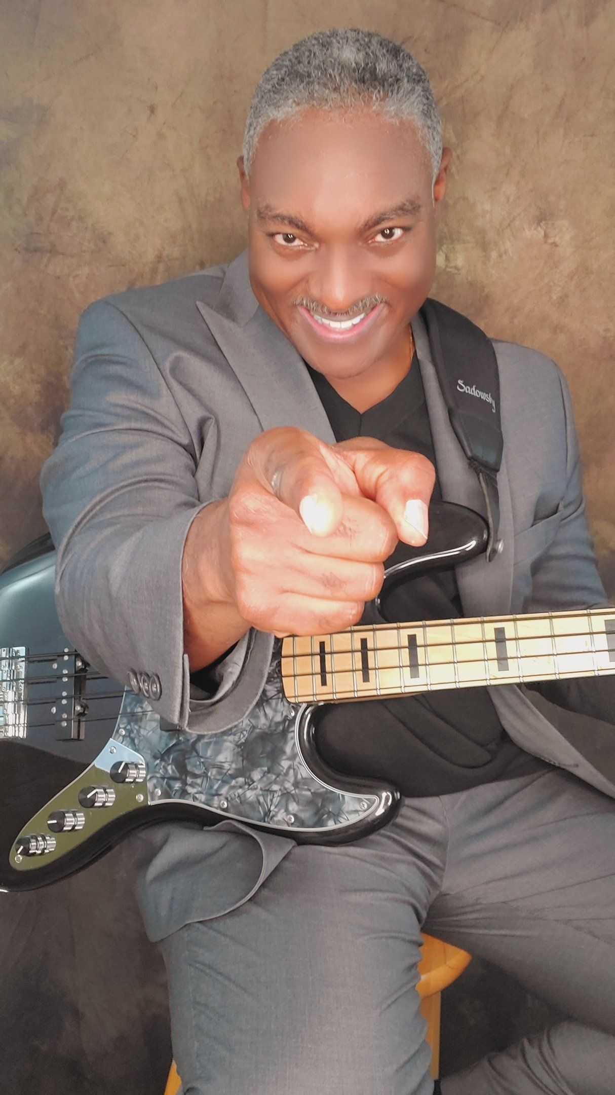 A man in a suit is holding a guitar and pointing at the camera.