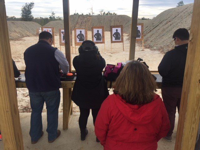 People shooting at targets at an outdoor gun range. Silhouette targets in the background.