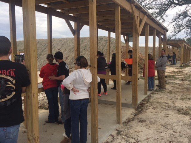 People shooting at a gun range, standing under a wooden shelter.