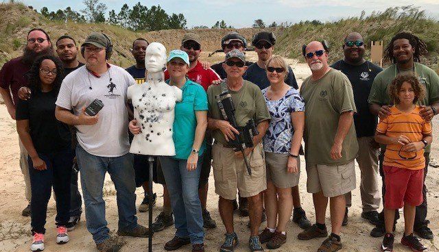 Group of people at an outdoor shooting range, posing with a target dummy.