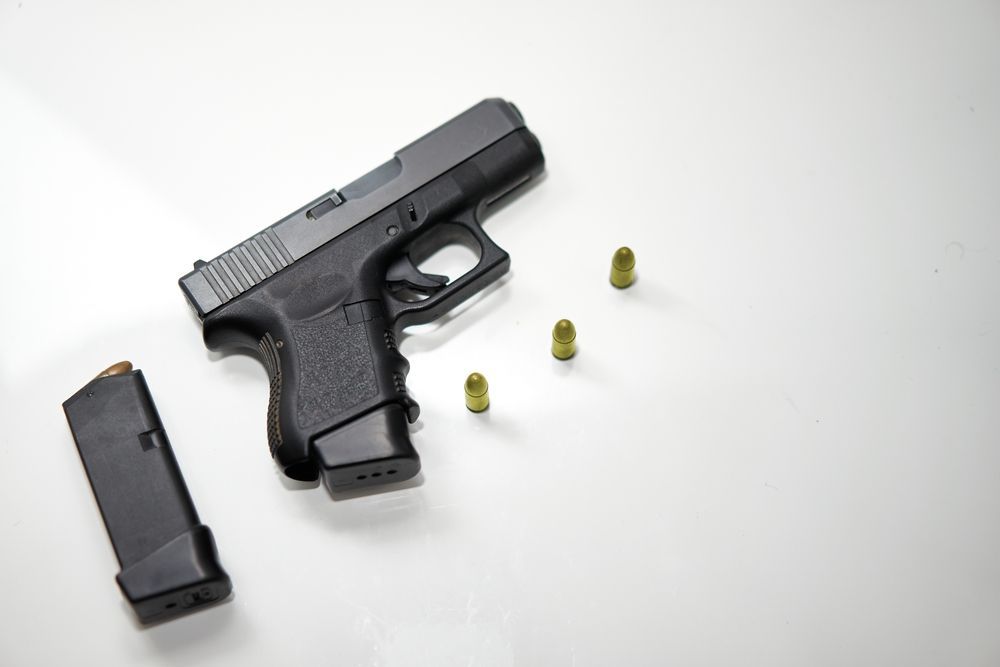 Black handgun with magazine and bullets on a white surface.