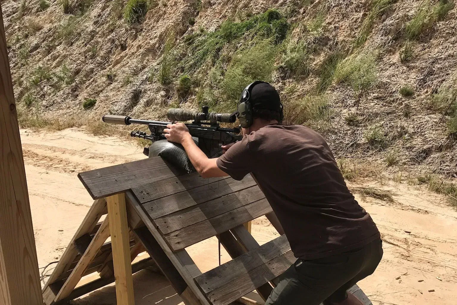 Person shooting rifle at outdoor range, using a bench rest.