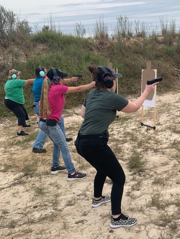 Four people shooting pistols at targets on an outdoor range.