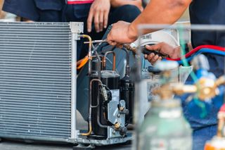 Technician repairing an HVAC unit with tools beside exposed wiring and coils.