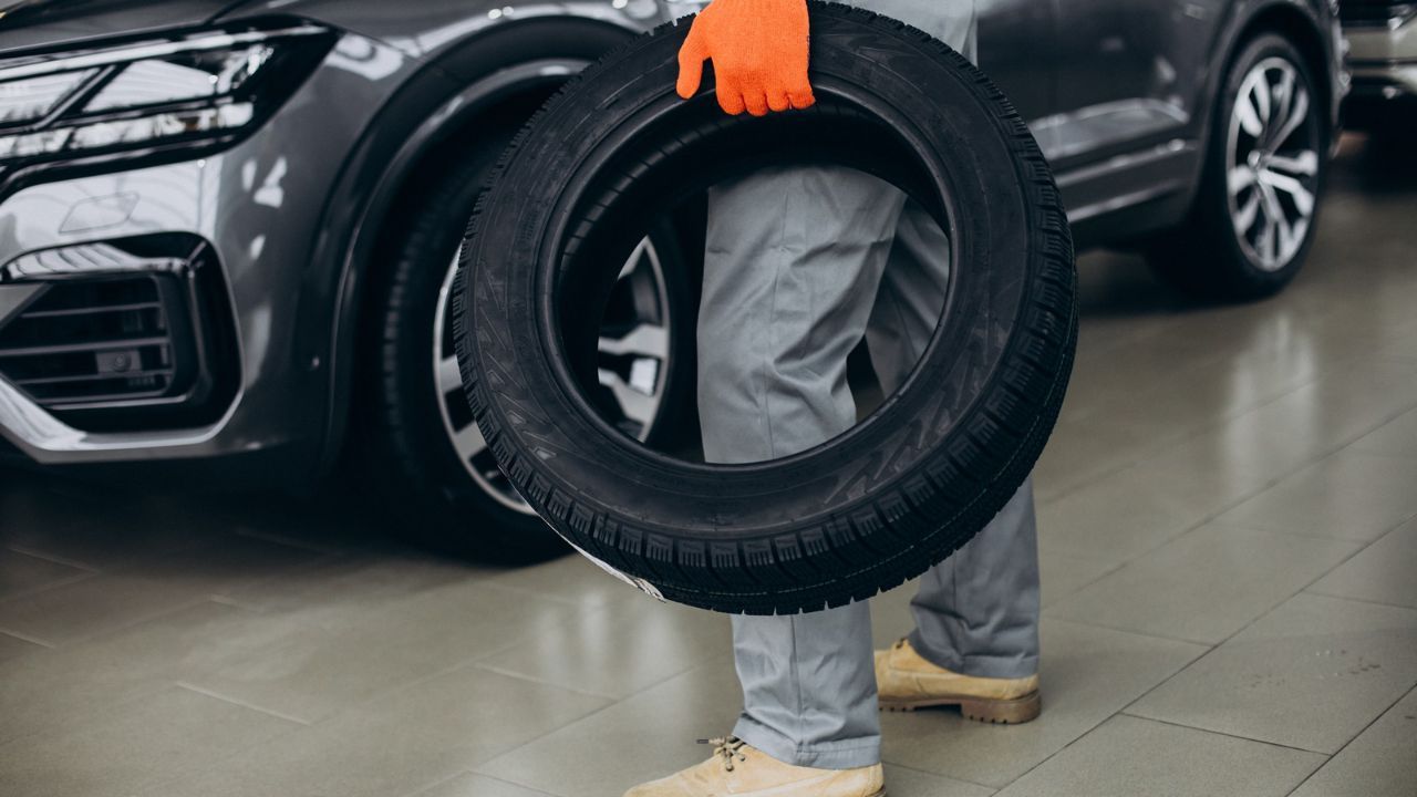 Auto technician carrying a replacement tire inside a vehicle service center