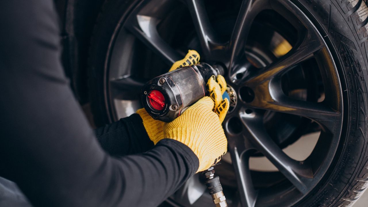 Mechanic using an impact wrench to remove lug nuts from a vehicle wheel