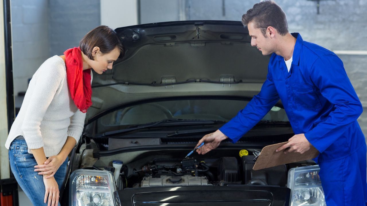 Auto mechanic explaining engine components to a customer during inspection.