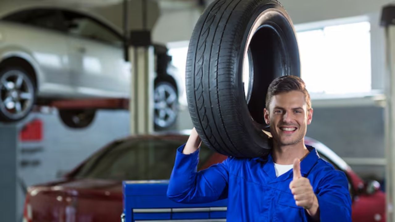 Auto mechanic holding a car tire on his shoulder
