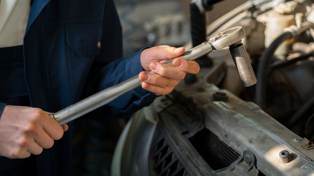 Mechanic tightening bolt with ratchet wrench inside car engine bay
