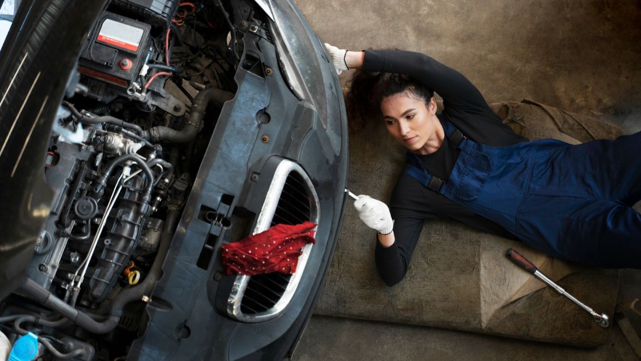 Mechanic lying under car inspecting engine components with tools
