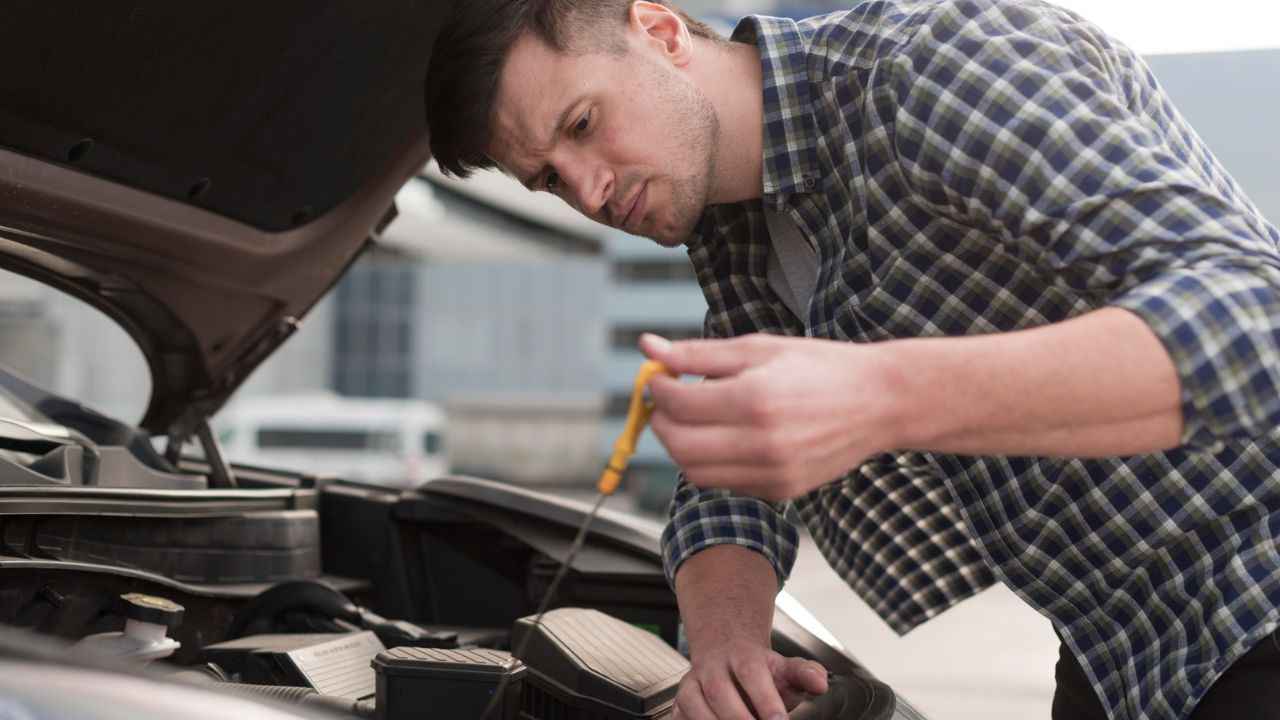  Man checking engine oil level with dipstick under car hood