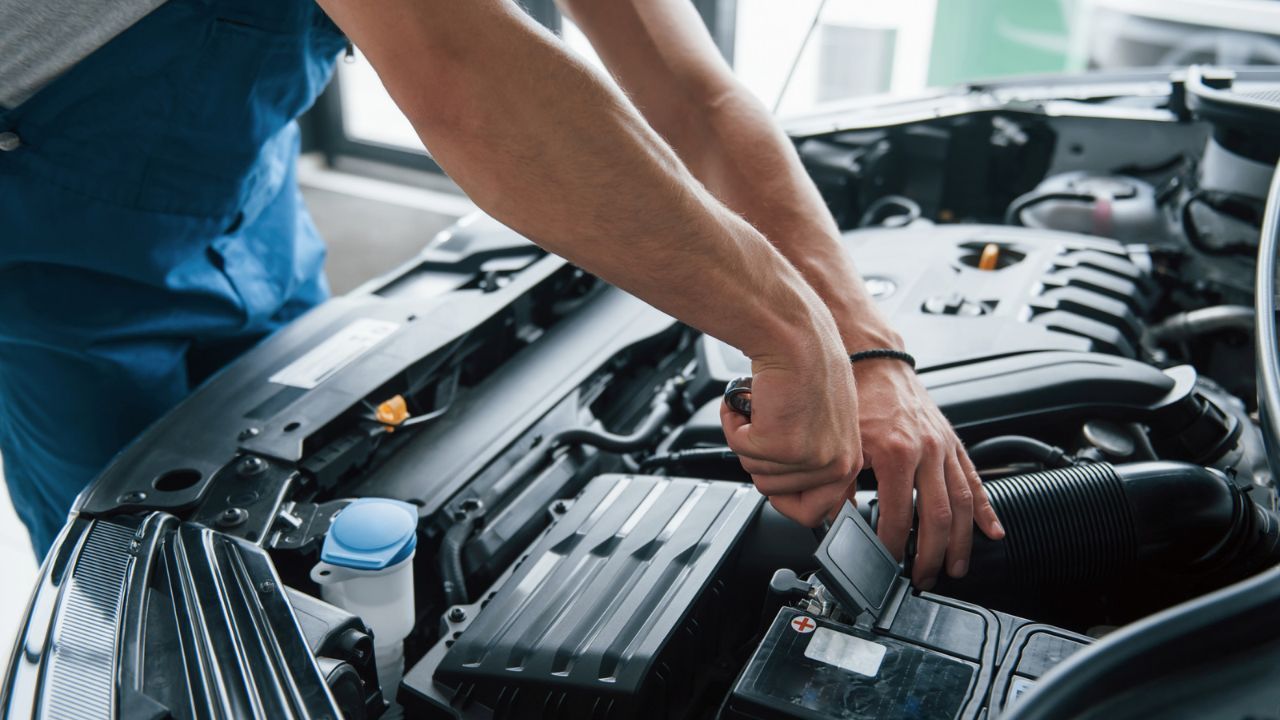 Auto technician installing a new car battery inside the engine bay during routine maintenance.