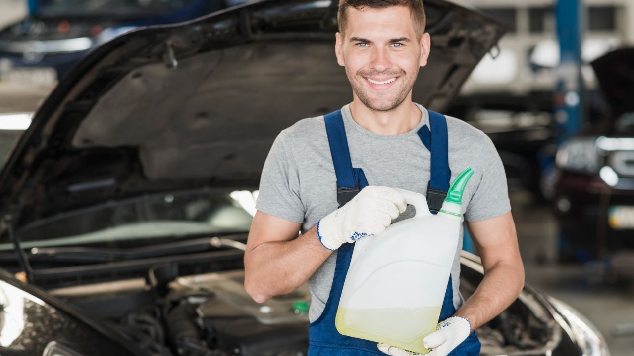 t: Auto technician holding fresh engine oil before performing a vehicle oil change.
