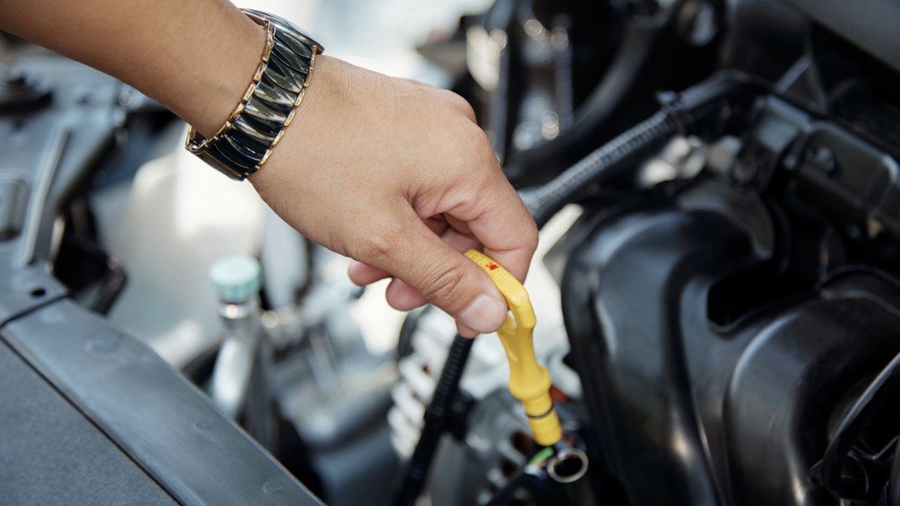  Gloved hand pulling out an engine oil dipstick to check the oil level inside a vehicle’s engine bay