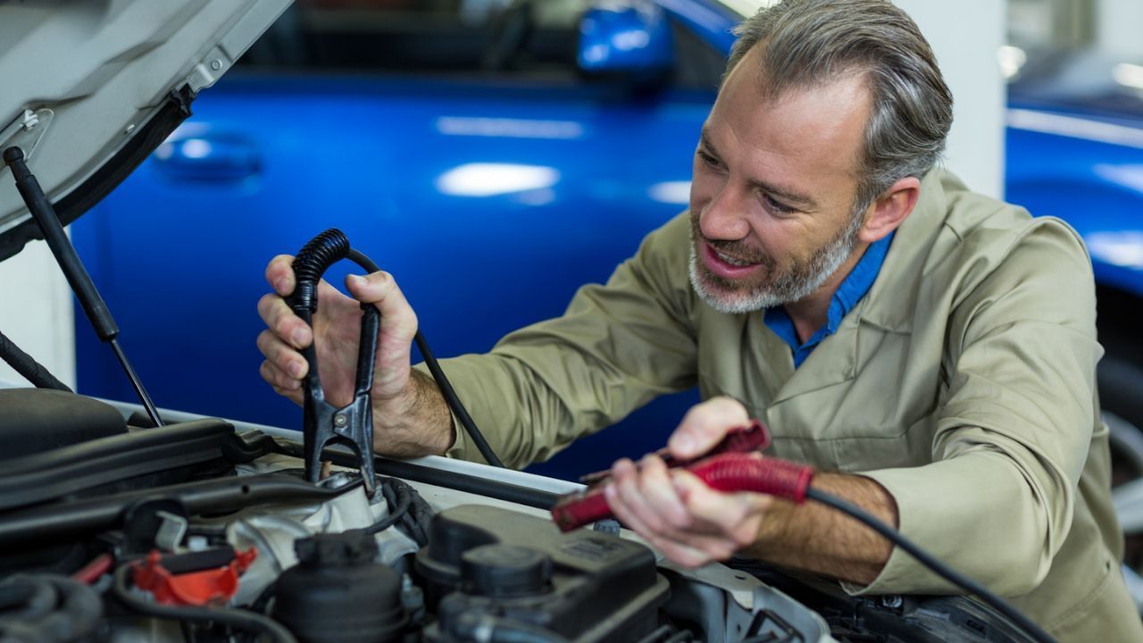 Mechanic using jumper cables to connect a car battery inside an open engine bay