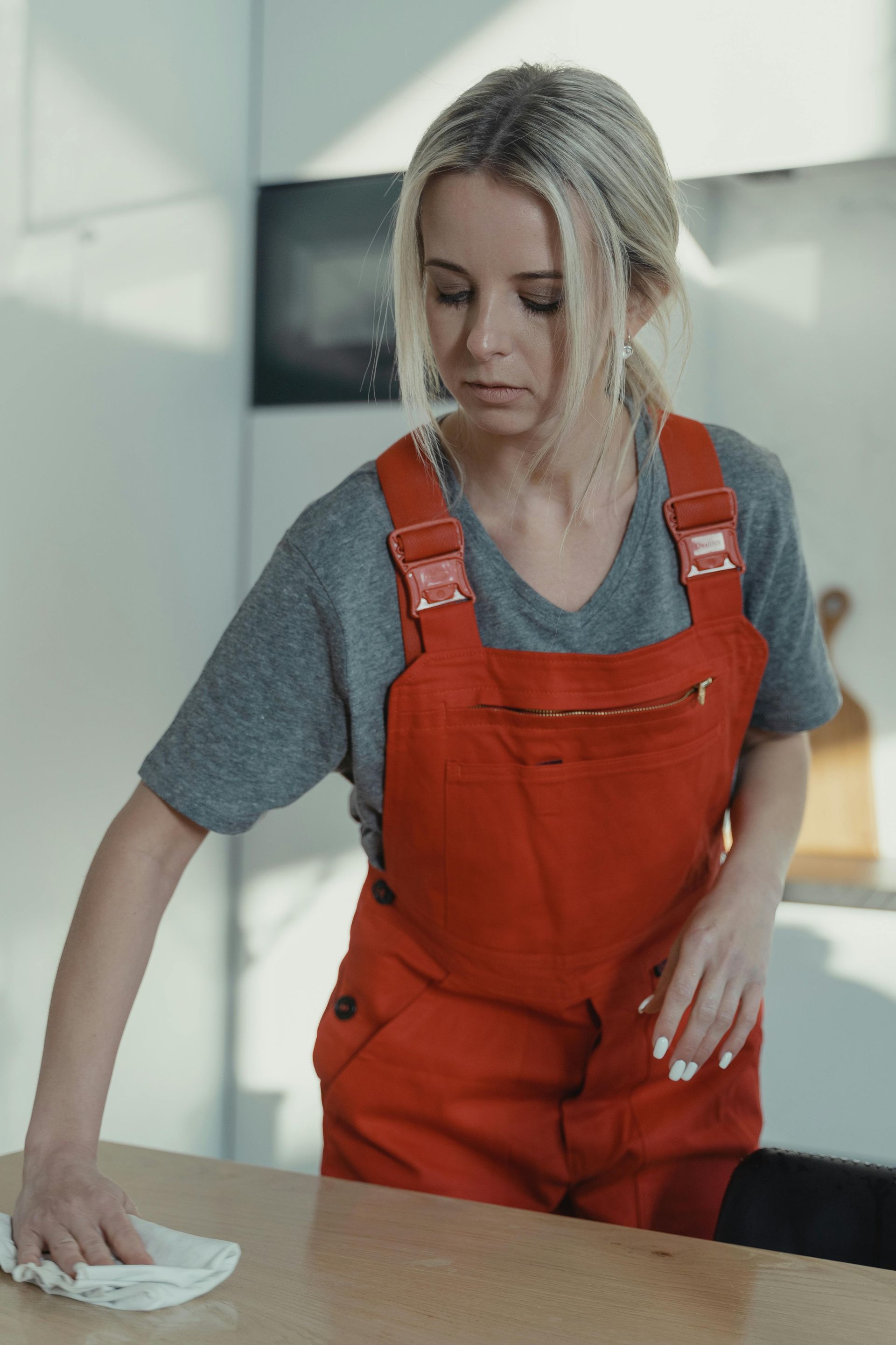 Woman in orange overalls wiping a table in a bright room