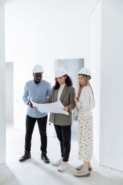 Three construction workers in hard hats reviewing a blueprint in a bright, empty room