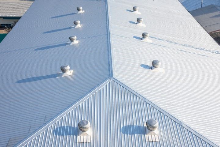 An aerial view of a symmetrical, light-colored corrugated metal roof featuring several evenly spaced roof turbine vents.