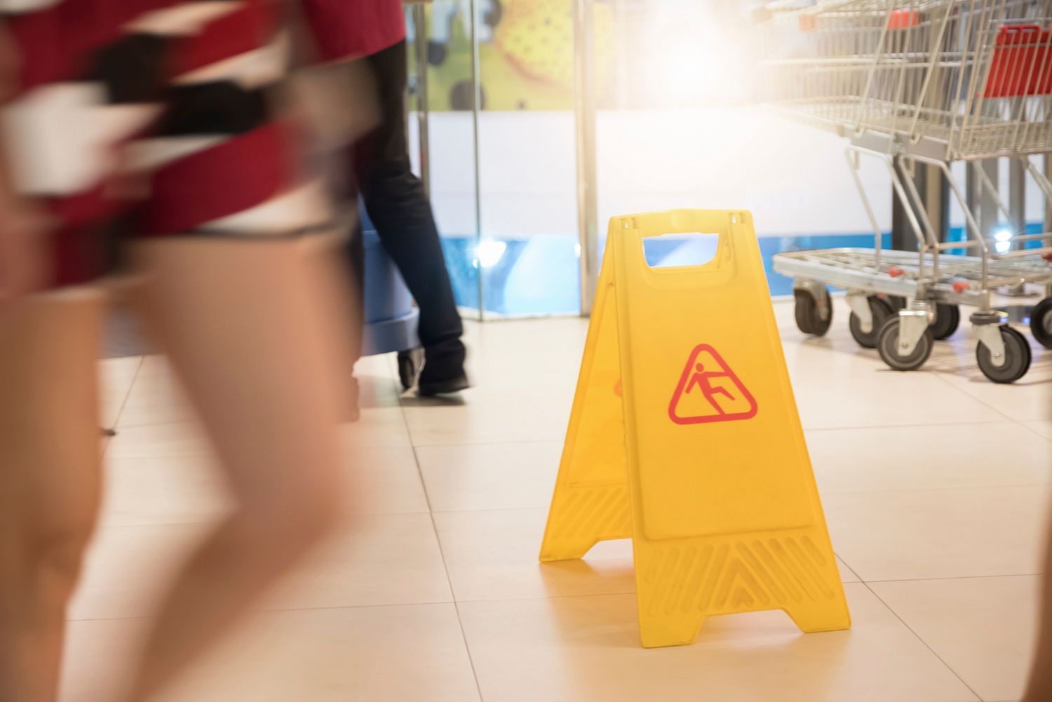 Yellow wet floor sign in a store, with blurry people walking past.