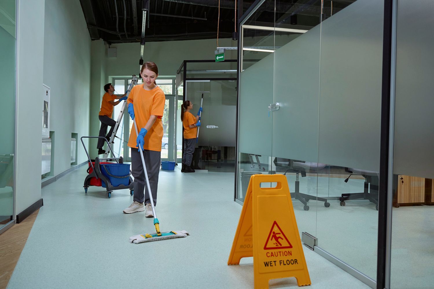Janitors cleaning an office. One mopping the floor; two others cleaning walls. Yellow
