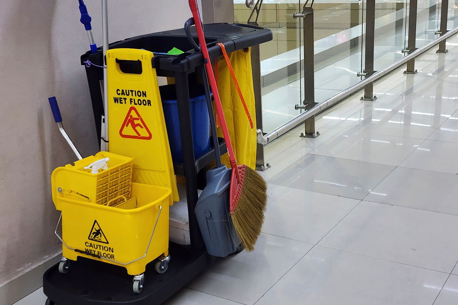 Cleaning cart with wet floor sign and supplies in a hallway. Cleaning cart with wet floor sign and supplies in a hallway.
