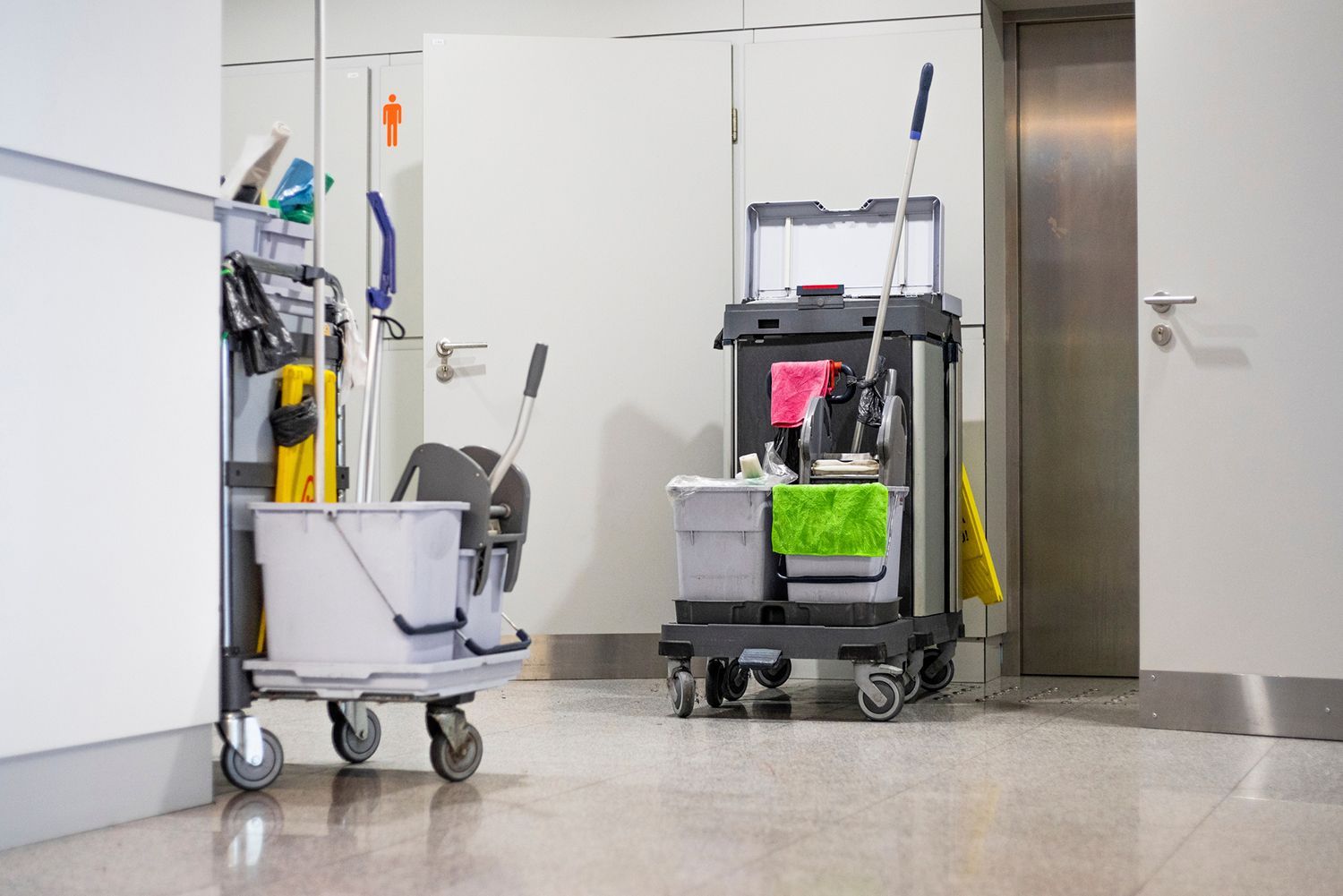 Two cleaning carts in a hallway with cleaning supplies and buckets. Two cleaning carts in a hallway with cleaning supplies and buckets.