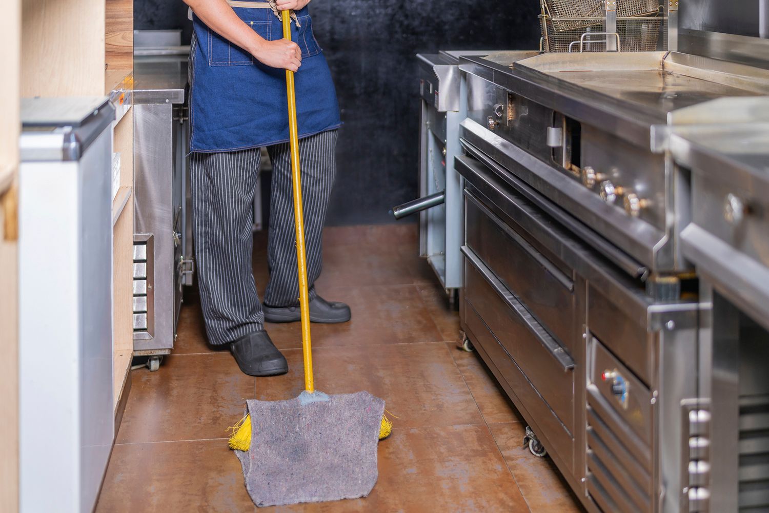 Person mopping a restaurant kitchen floor. Person mopping a restaurant kitchen floor.