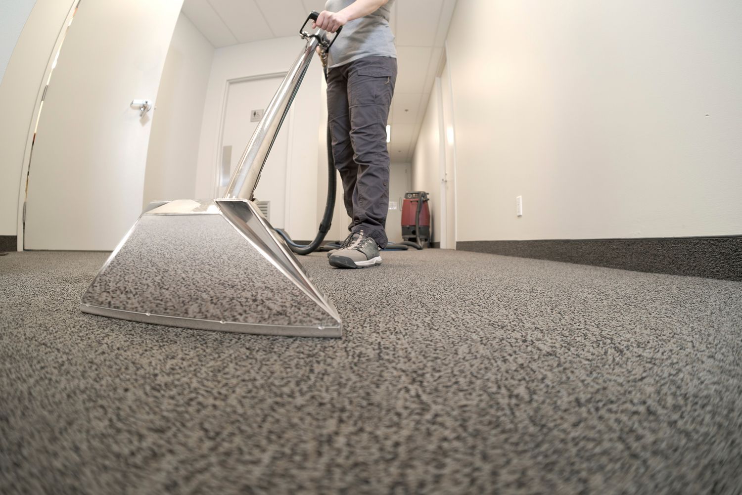 Person cleaning a hallway carpet with an industrial carpet cleaner. Person cleaning a hallway carpet with an industrial carpet cleaner.