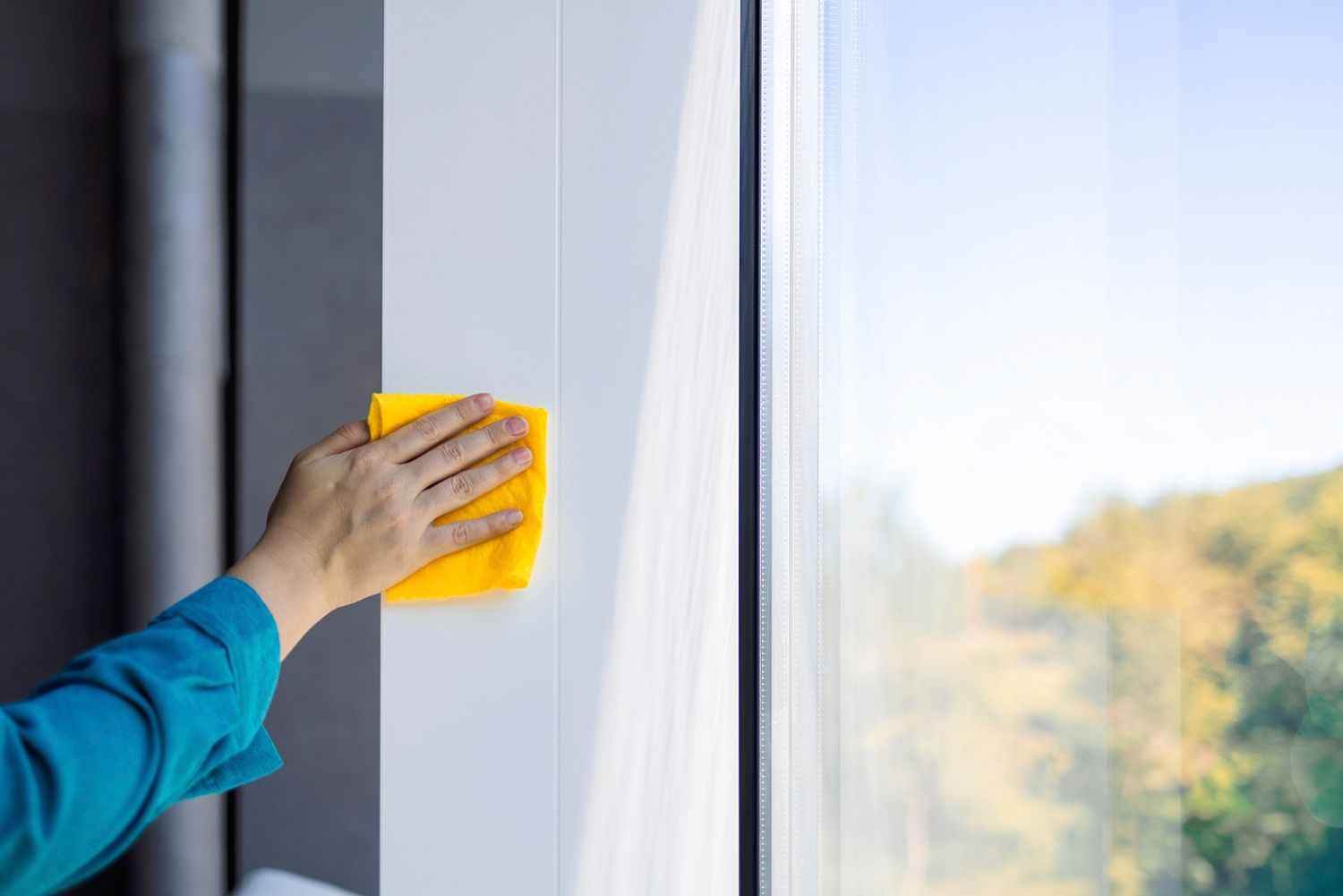 Person cleaning a white window frame with a yellow cloth. Sunlight through the window. Person cleaning a white window frame with a yellow cloth. Sunlight through the window.