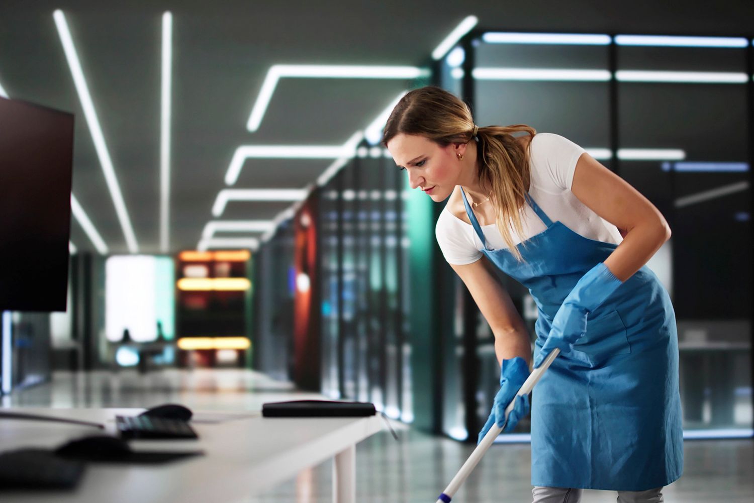 Woman in blue apron and gloves mopping a white desk in an office. Woman in blue apron and gloves mopping a white desk in an office.