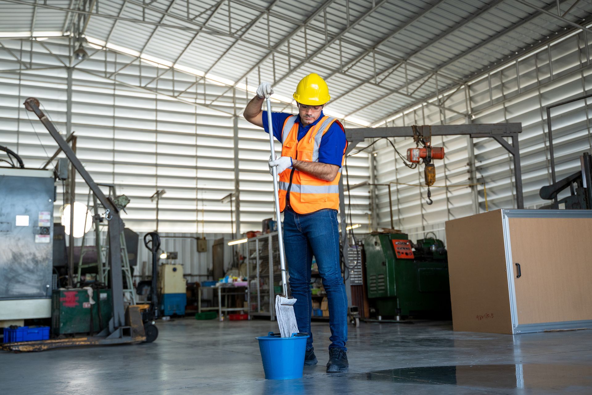 Two people mopping a brightly lit office hallway. They wear blue coveralls and yellow gloves. Two people mopping a brightly lit office hallway. They wear blue coveralls and yellow gloves.