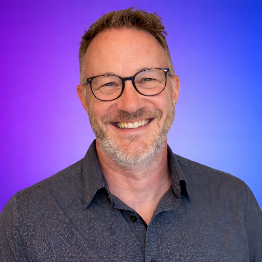 Man with glasses smiling, wearing a dark shirt, purple background.
