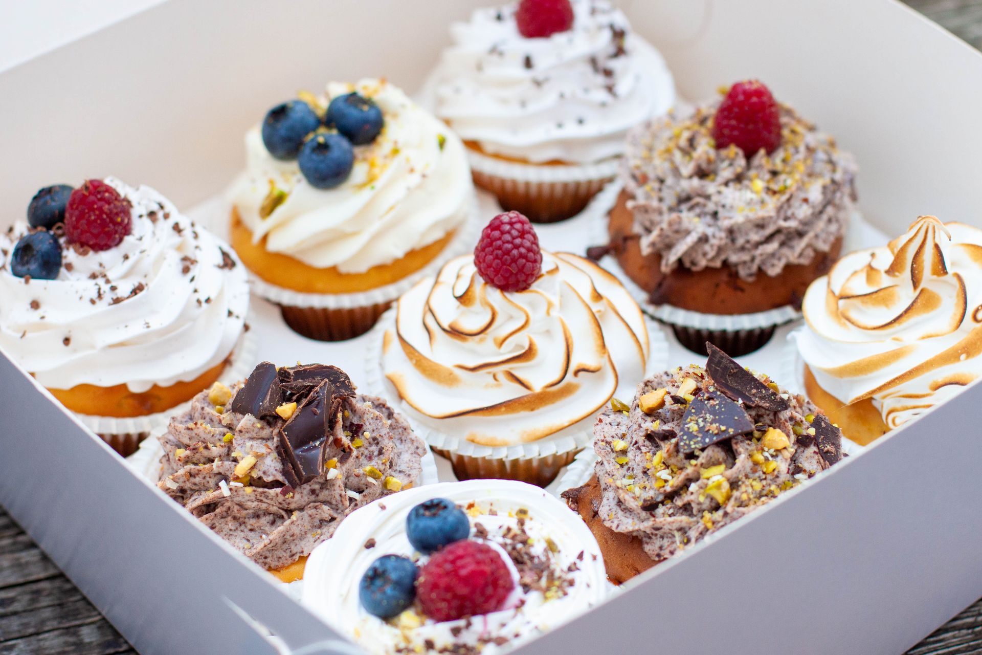 Una scatola piena di cupcakes con guarnizioni diverse.