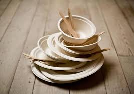 Una pila di piatti e ciotole di carta con cucchiai di legno su un tavolo di legno.