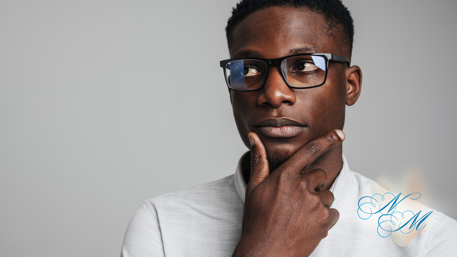 Man wearing glasses, holding chin, looking thoughtful, against a gray background.