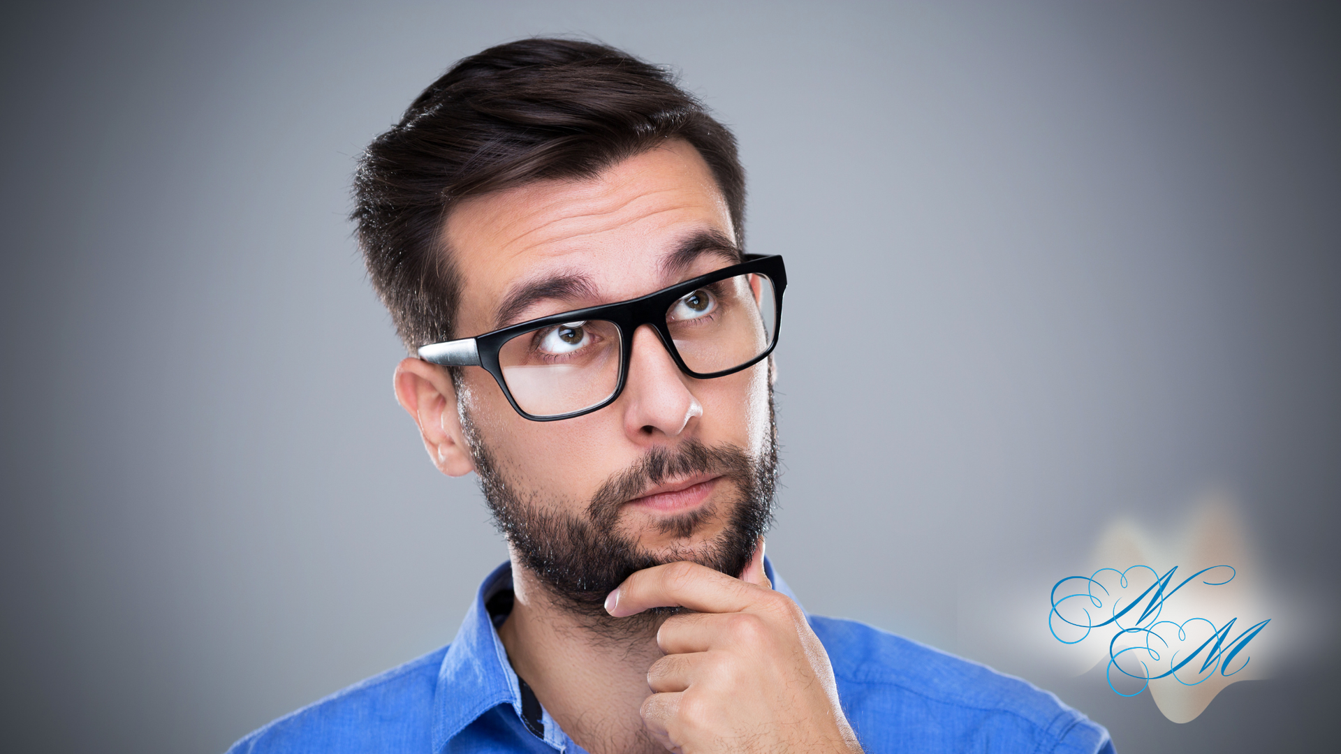 Man with glasses looks up thoughtfully, hand on chin, against a gray background.