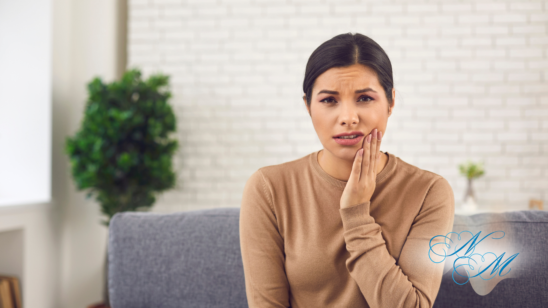 Woman on sofa holding cheek, appearing in pain, indoors.